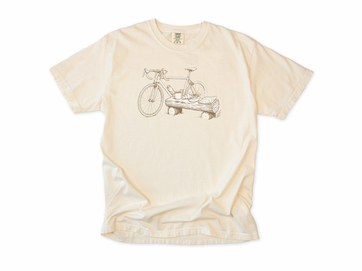 Funny cycling T-shirt in Ivory, a bike propped on a log with a drink, for gravel and trail riders