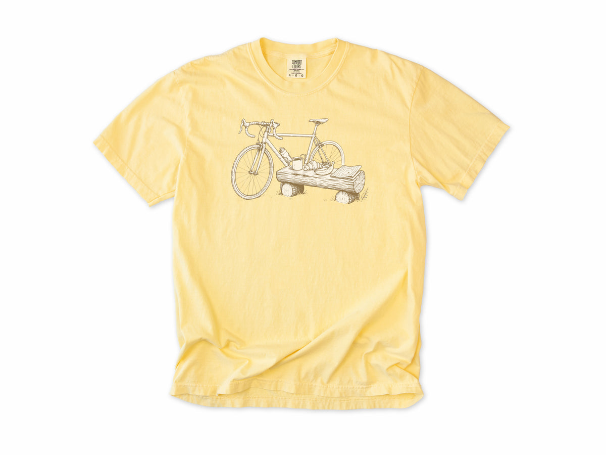 Funny cycling T-shirt in Butter, a bike propped on a log with a drink, for gravel and trail riders