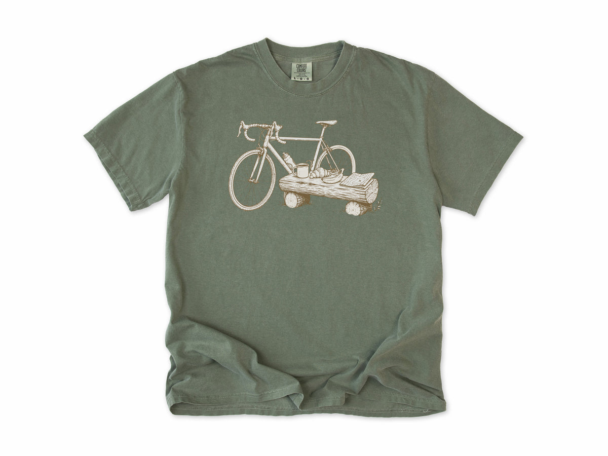 Funny cycling T-shirt in Moss, a bike propped on a log with a drink, for gravel and trail riders