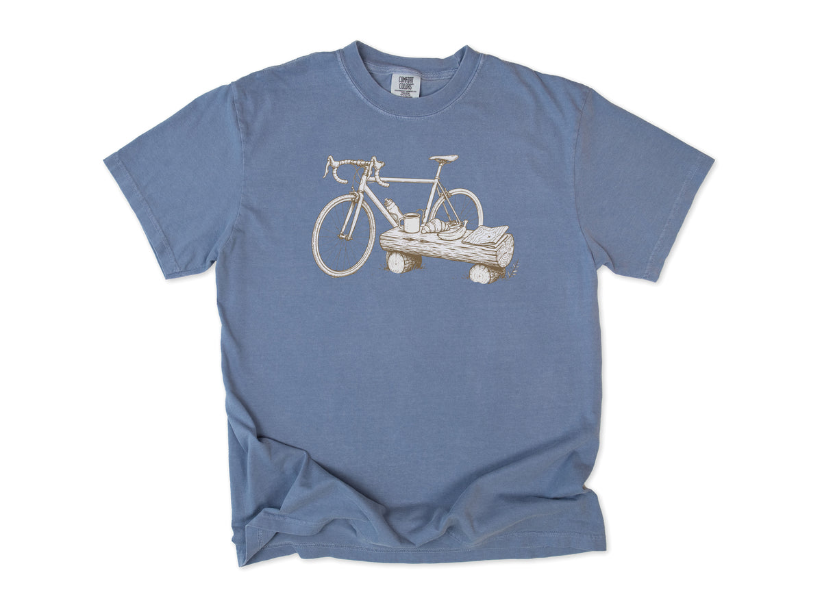 Funny cycling T-shirt in Blue Jean, a bike propped on a log with a drink, for gravel and trail riders