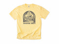 Cycling T-shirt in Butter, a woodcut cyclist on a country road, 'Adventure Awaits', for touring and leisure cyclists