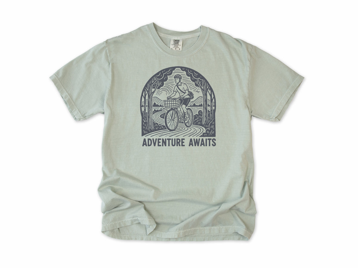 Cycling T-shirt in Bay, a woodcut cyclist on a country road, 'Adventure Awaits', for touring and leisure cyclists