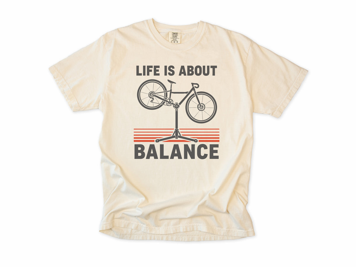 Funny cycling T-shirt in Ivory, 'Life Is About Balance' with a bike on a repair stand, for cyclists and bike mechanics