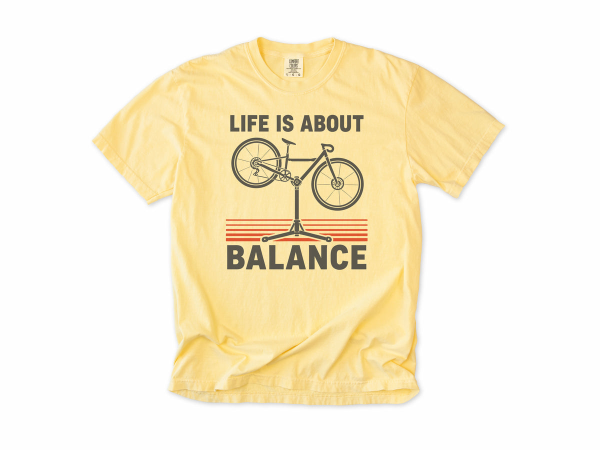 Funny cycling T-shirt in Butter, 'Life Is About Balance' with a bike on a repair stand, for cyclists and bike mechanics