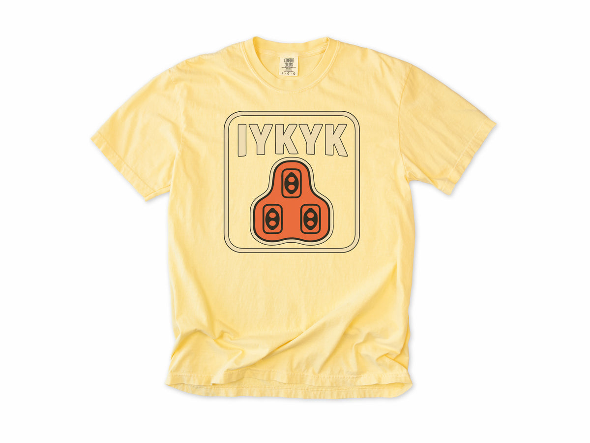 Funny cycling T-shirt in Butter, 'IYKYK' with an orange road bike cleat, for riders who use clipless pedals