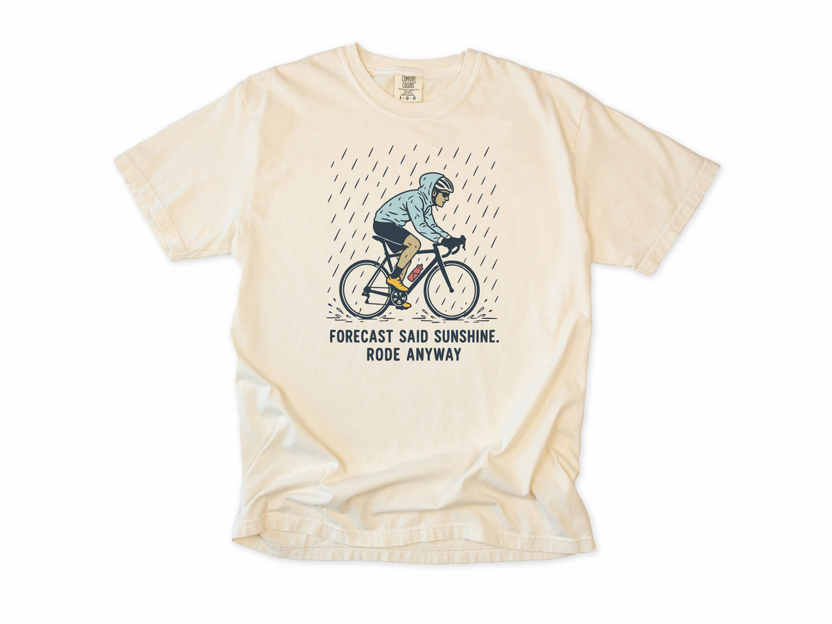Funny cycling T-shirt in Ivory, a cyclist in the rain, 'Forecast said sunshine. Rode anyway', for all-weather riders