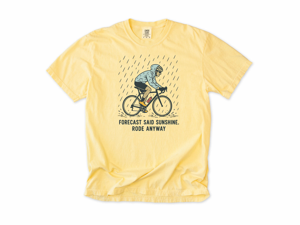Funny cycling T-shirt in Butter, a cyclist in the rain, 'Forecast said sunshine. Rode anyway', for all-weather riders