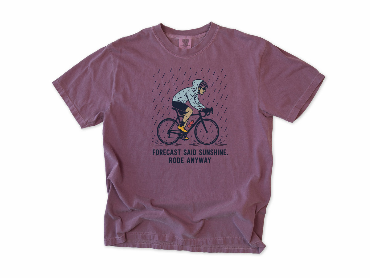 Funny cycling T-shirt in Berry, a cyclist in the rain, 'Forecast said sunshine. Rode anyway', for all-weather riders