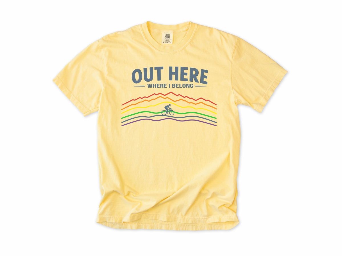 Cycling T-shirt in Butter, 'Out Here Where I Belong' with rainbow mountain lines and a cyclist, for outdoor cyclists