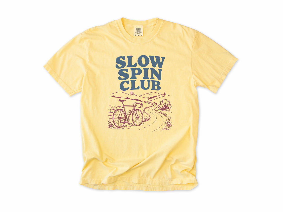 Cycling T-shirt in Butter, 'Slow Spin Club' with a bike on a winding country lane, for relaxed riders