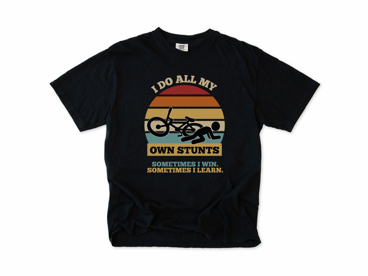 Funny cycling T-shirt in Black, 'I Do All My Own Stunts', a crashed rider on retro sunset stripes, for mountain bikers