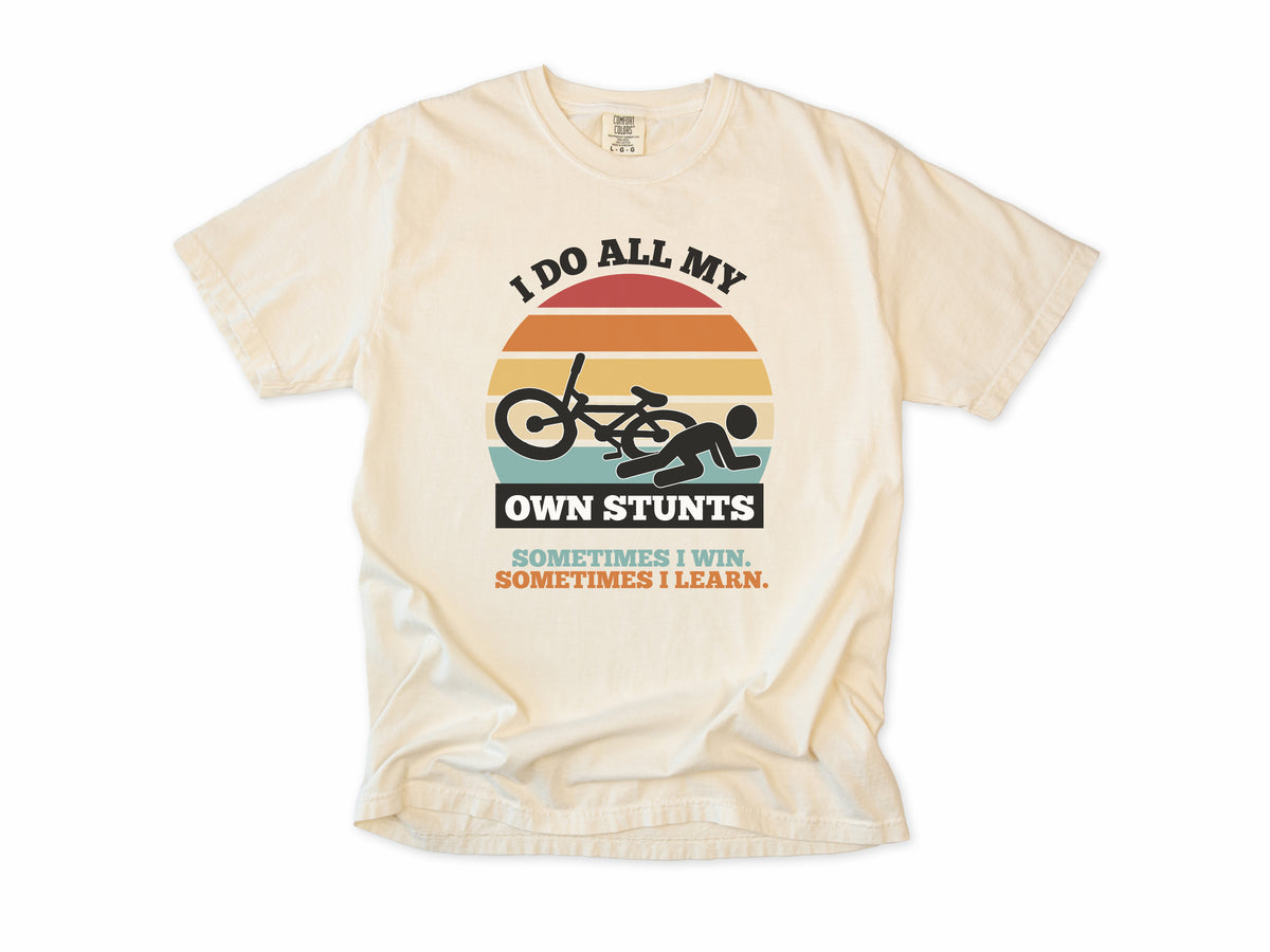 Funny cycling T-shirt in Ivory, 'I Do All My Own Stunts', a crashed rider on retro sunset stripes, for mountain bikers