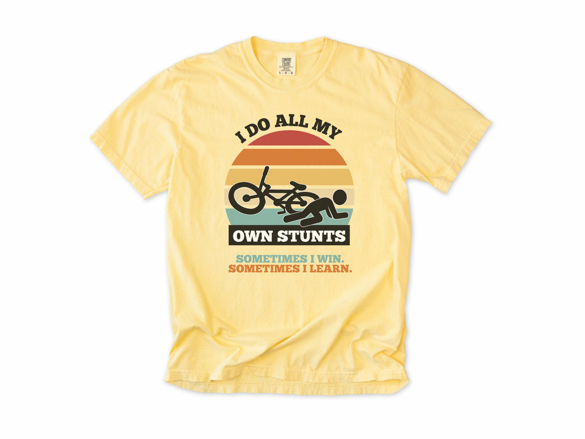 Funny cycling T-shirt in Butter, 'I Do All My Own Stunts', a crashed rider on retro sunset stripes, for mountain bikers