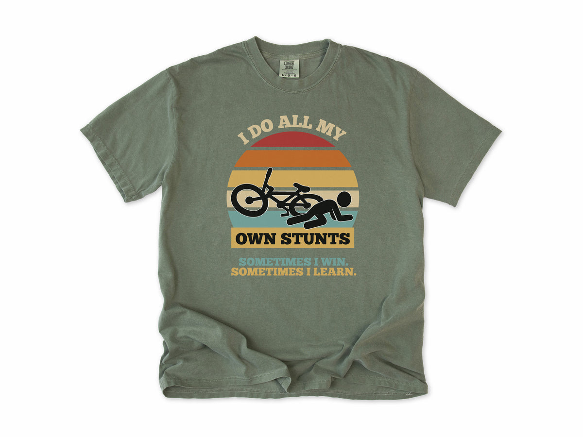 Funny cycling T-shirt in Moss, 'I Do All My Own Stunts', a crashed rider on retro sunset stripes, for mountain bikers
